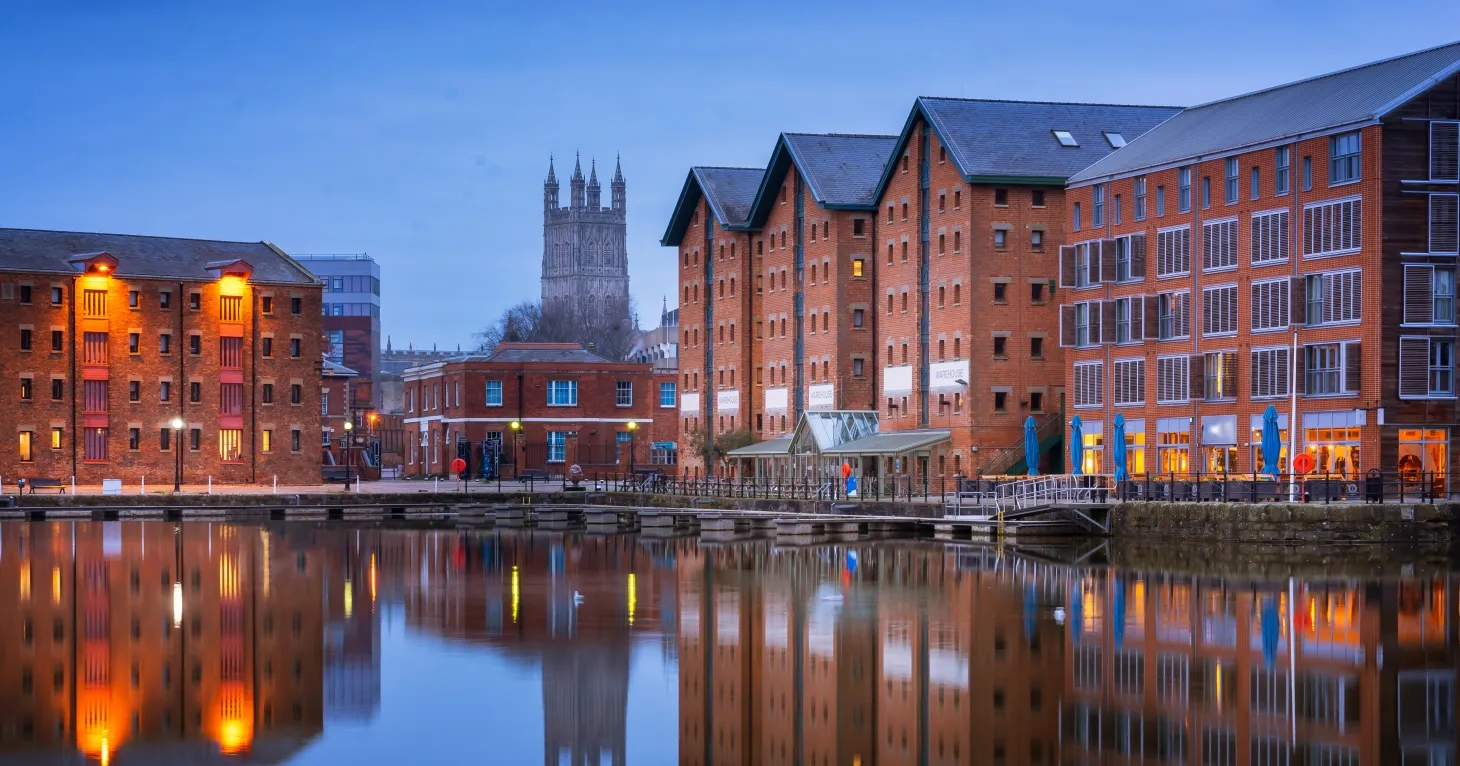 Gloucester Docks at dusk, with the warehouses reflected in the water and Gloucester Cathedral tower behind